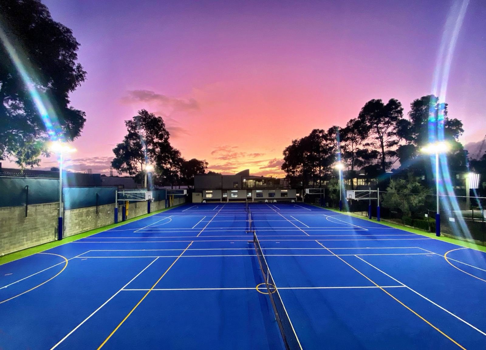 Floodlit tennis courts at Bialik College beneath a pink sunset